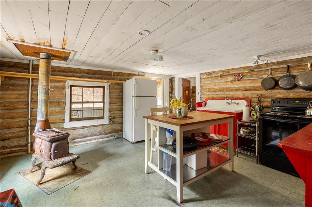 Rustic kitchen with log walls, a wood-burning stove, red farmhouse sink, and central island.