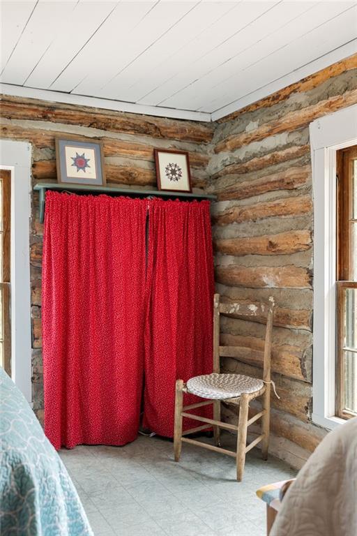 Log cabin bedroom with exposed log walls, a bright red curtain, and a wooden chair.
