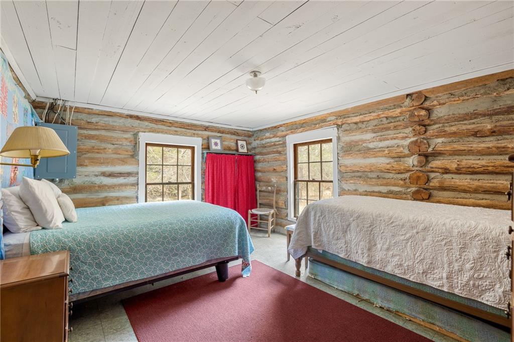 Rustic log cabin bedroom with two beds, exposed log walls, and a red curtain.