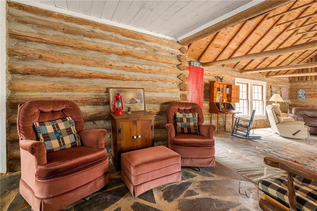 Rustic log cabin living room with exposed beams, stone flooring, and reddish-brown armchairs.