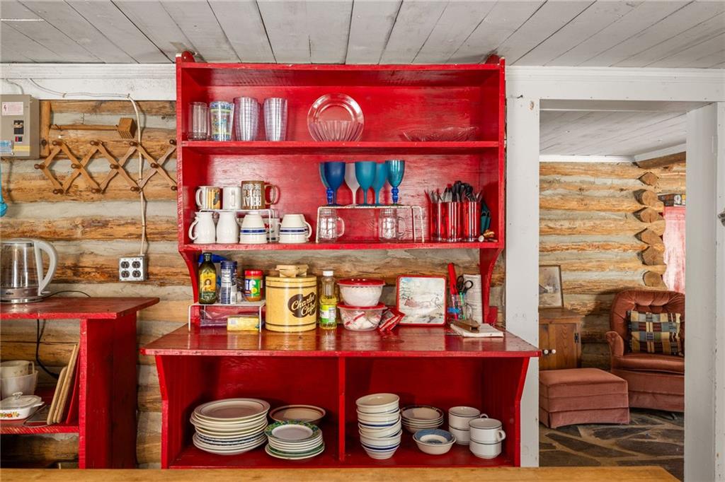 Rustic log cabin kitchen with a bright red dish hutch and a view into the adjoining sitting area.