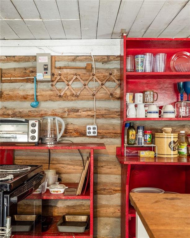 Rustic log cabin kitchen with red shelves, a small stove, and exposed log walls.