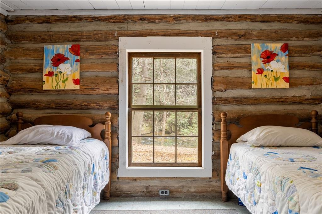 Rustic log-cabin bedroom with twin beds flanking a window overlooking trees.