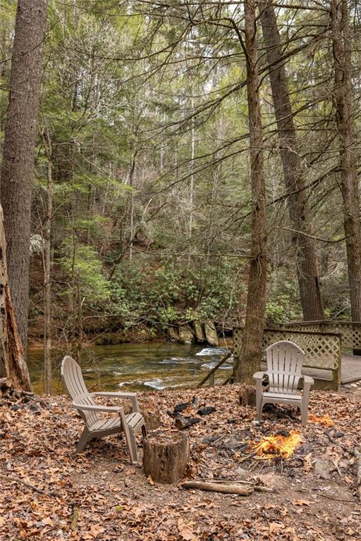 Woodland seating area with Adirondack chairs and a fire pit beside a creek.