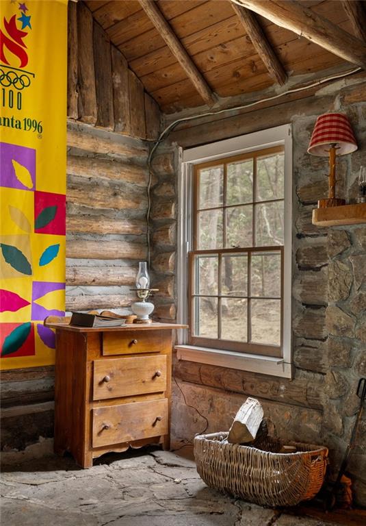 Rustic cabin interior with exposed beams, a tall wooded-view window, and an Atlanta 1996 banner.