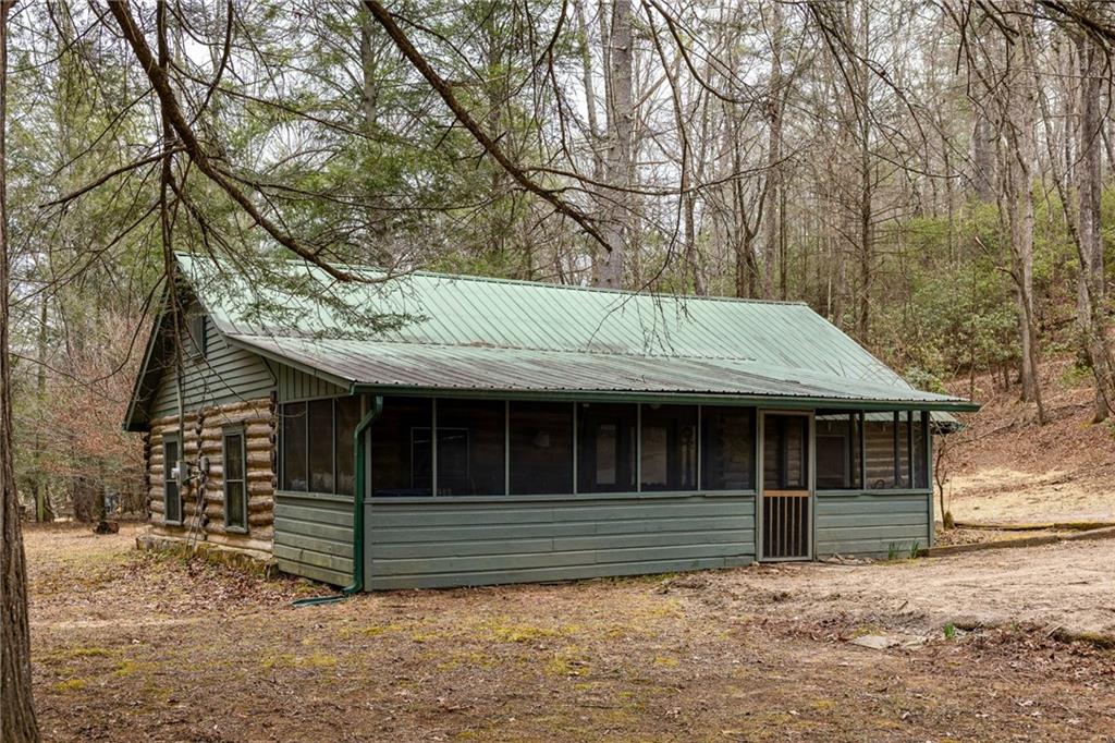 Log-sided cabin with a pale green metal roof and long screened porch among leafless trees.