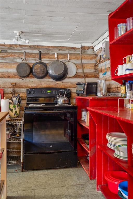 Rustic kitchen with log walls, a black stove, hanging pans, and bright red shelves filled with dishes.