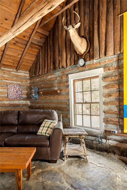 Rustic log-cabin living room with exposed rafters, leather sofa, stone floor, and mounted deer head.