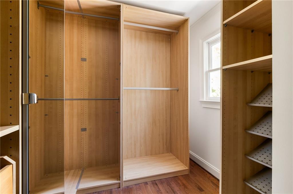 Walk-in closet with light wood shelving, glass sliding doors, and hardwood flooring.