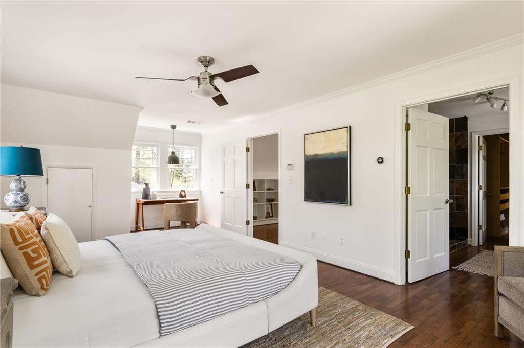 Furnished bedroom with a white bed, striped bedding, hardwood floors, and a desk by the windows.
