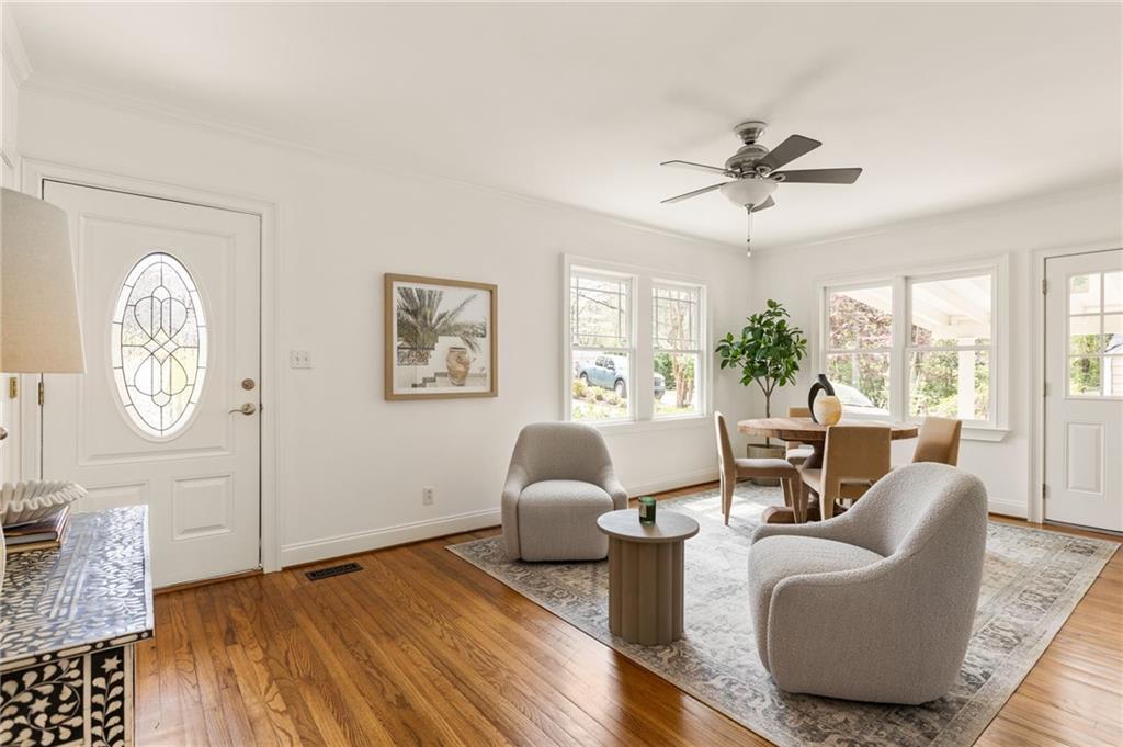 Living and dining area with hardwood floors, upholstered chairs, large windows, and a decorative glass front door.
