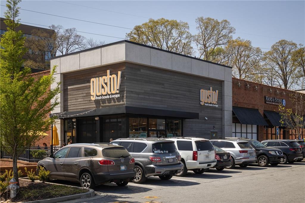 Commercial storefront with Gusto! signage, neighboring shops, and cars parked in front.