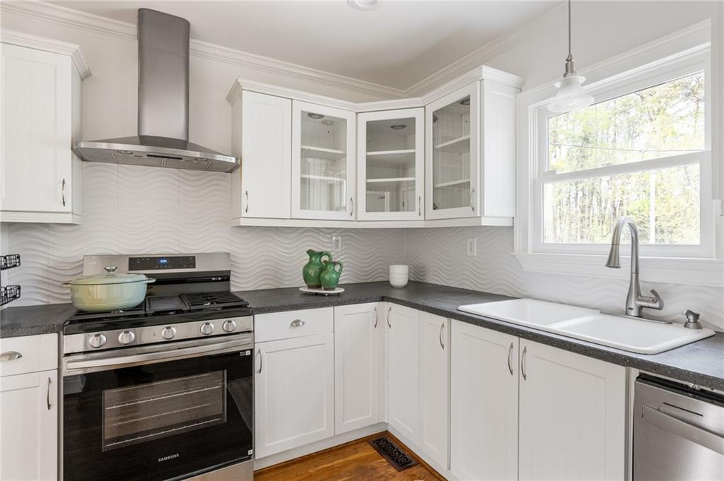 Bright white kitchen with a wavy backsplash, stainless steel range, and sink beneath a tree-facing window.