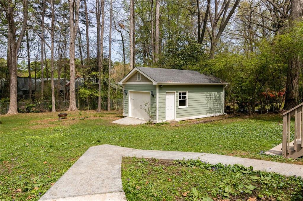 Pale green detached garage with a white garage door in a wooded backyard.