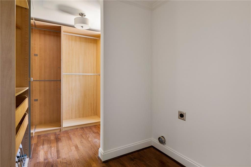 Walk-in closet with built-in wood shelving and drawers beside an empty hardwood-floored room.