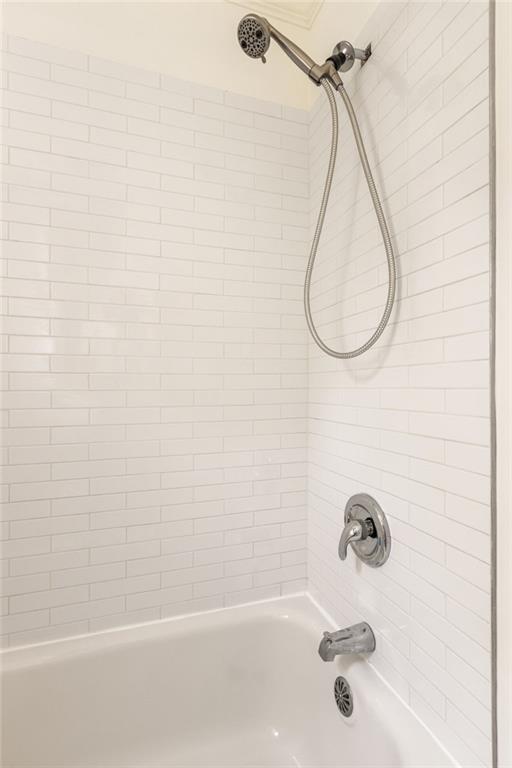 White subway-tile bathtub and shower with a chrome handheld showerhead and fixtures.