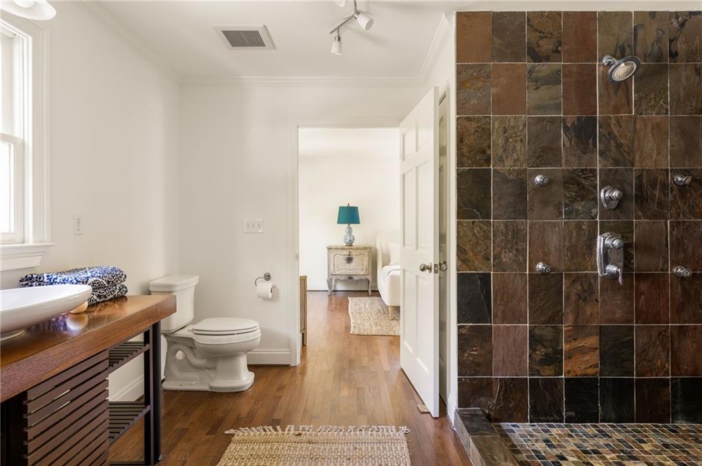 Bathroom with a dark slate-tile shower, wooden vanity, and doorway to an adjoining room.