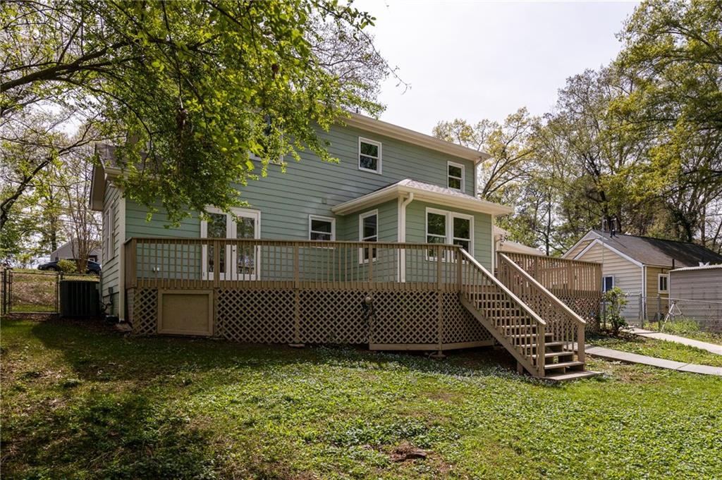 Rear of a green two-story home with a raised deck and stairs overlooking a grassy yard.
