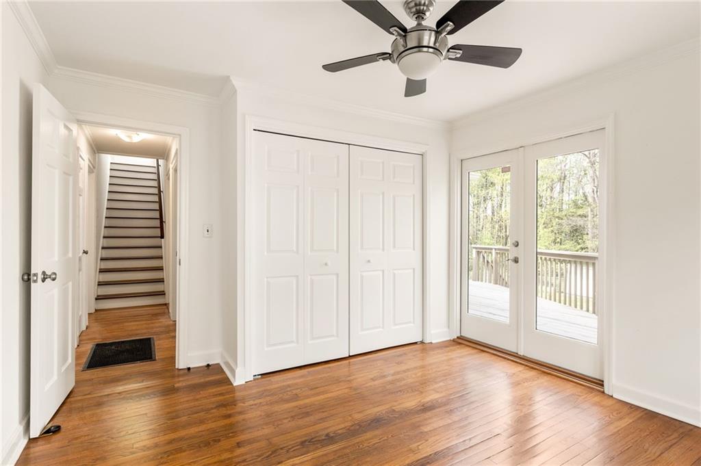 Vacant bedroom with hardwood floors, a ceiling fan, and glass doors to a wooded deck.