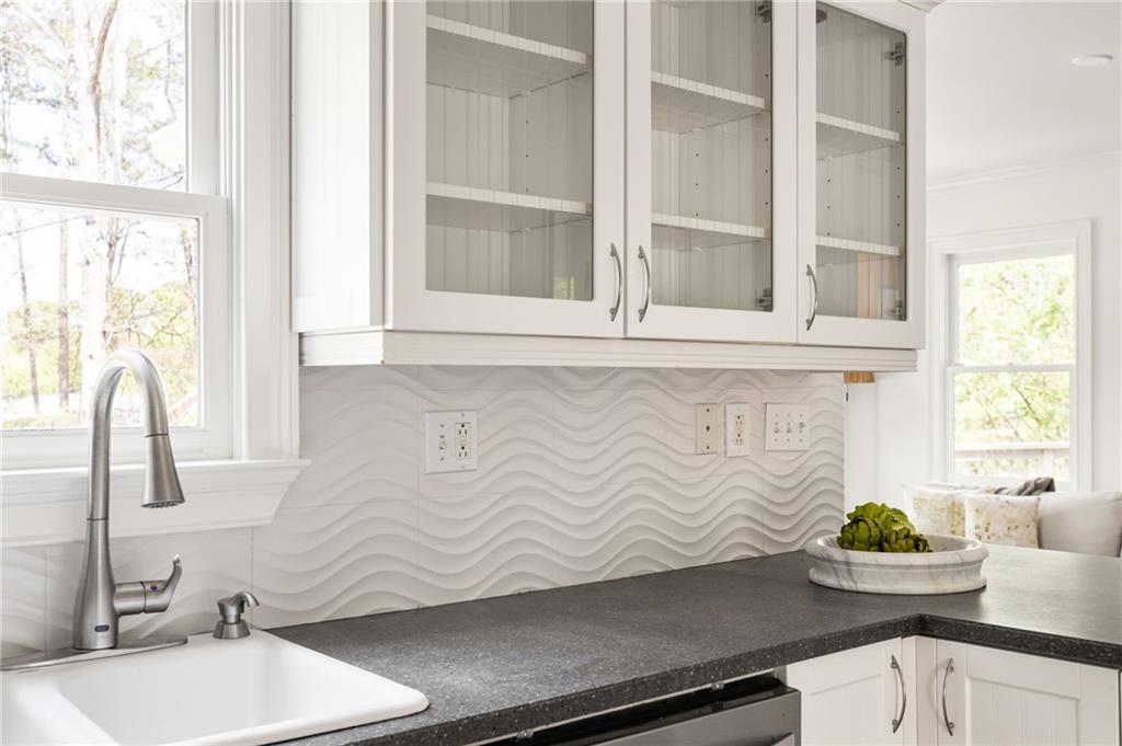 Bright kitchen with a wave-pattern backsplash, glass-front cabinets, and a deep sink beneath a window.