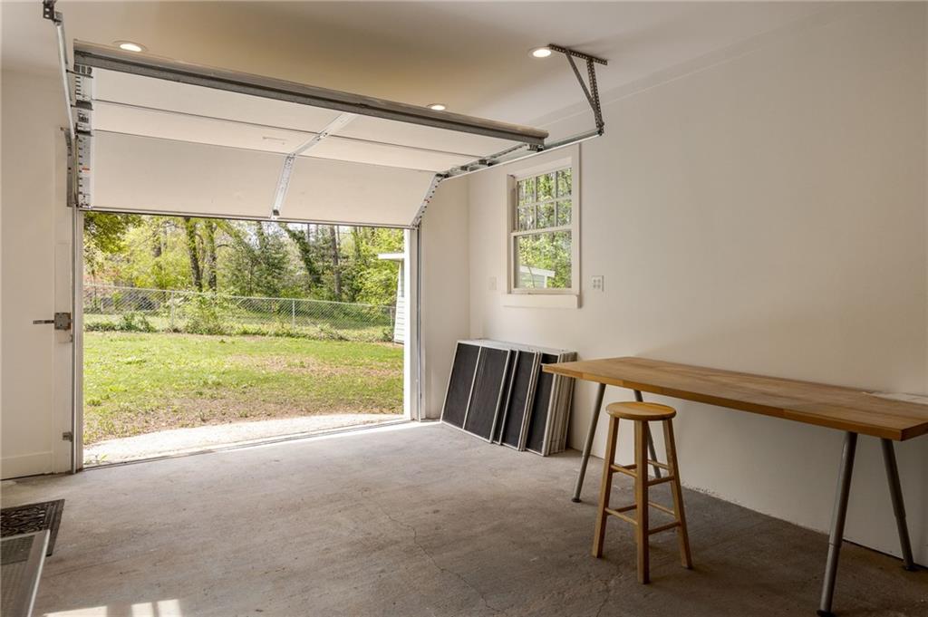 Garage with an open overhead door, wooden worktable, and view of a grassy fenced yard.