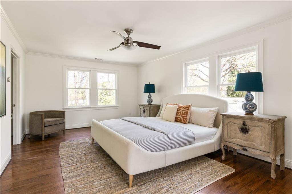 Bright bedroom with a white upholstered bed, striped bedding, and windows on two walls.