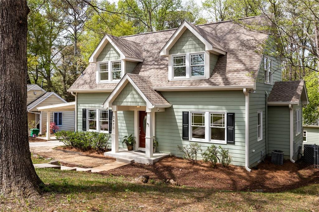 Sage-green two-story home with white-trimmed dormers and a covered front entry beneath mature trees.