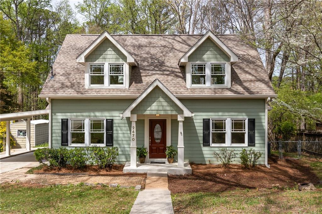 Sage-green two-story house with twin dormers, covered entry, and a walkway leading to the front door.