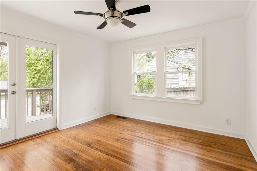 Vacant room with hardwood floors, a black ceiling fan, and a glass door opening to a deck.