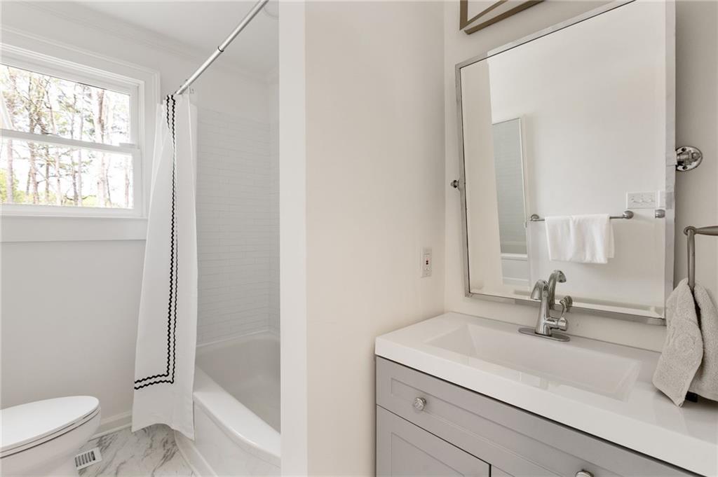 Bright bathroom with a white vanity, large mirror, and bathtub beside a window.