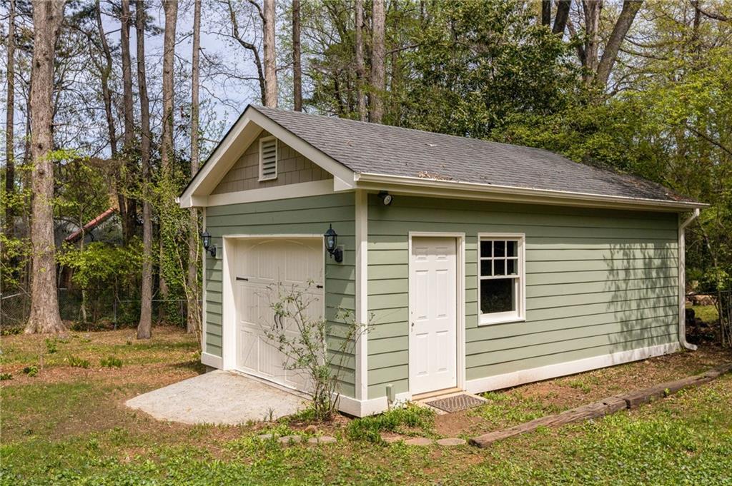 Detached green garage with white garage door, side entry, and window among trees.