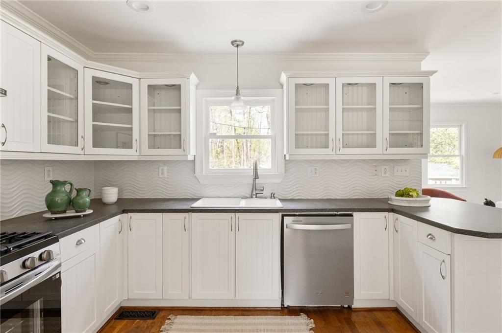 Bright kitchen with white glass-front cabinets, dark counters, wavy backsplash, and stainless steel appliances.
