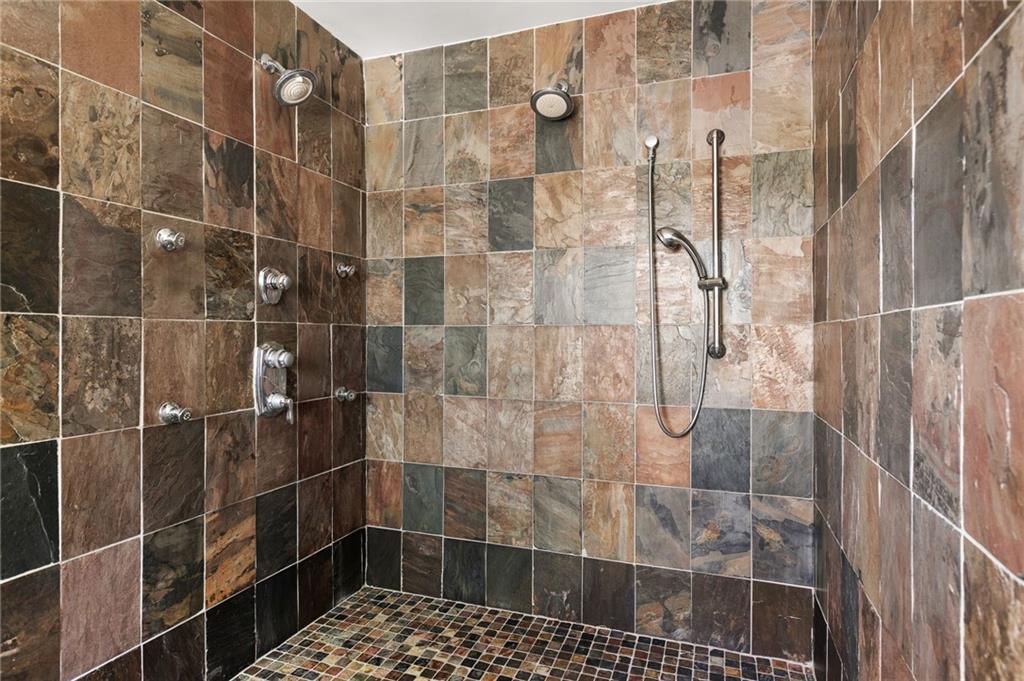 Walk-in shower with multicolored stone tile, two fixed showerheads and a handheld wand.