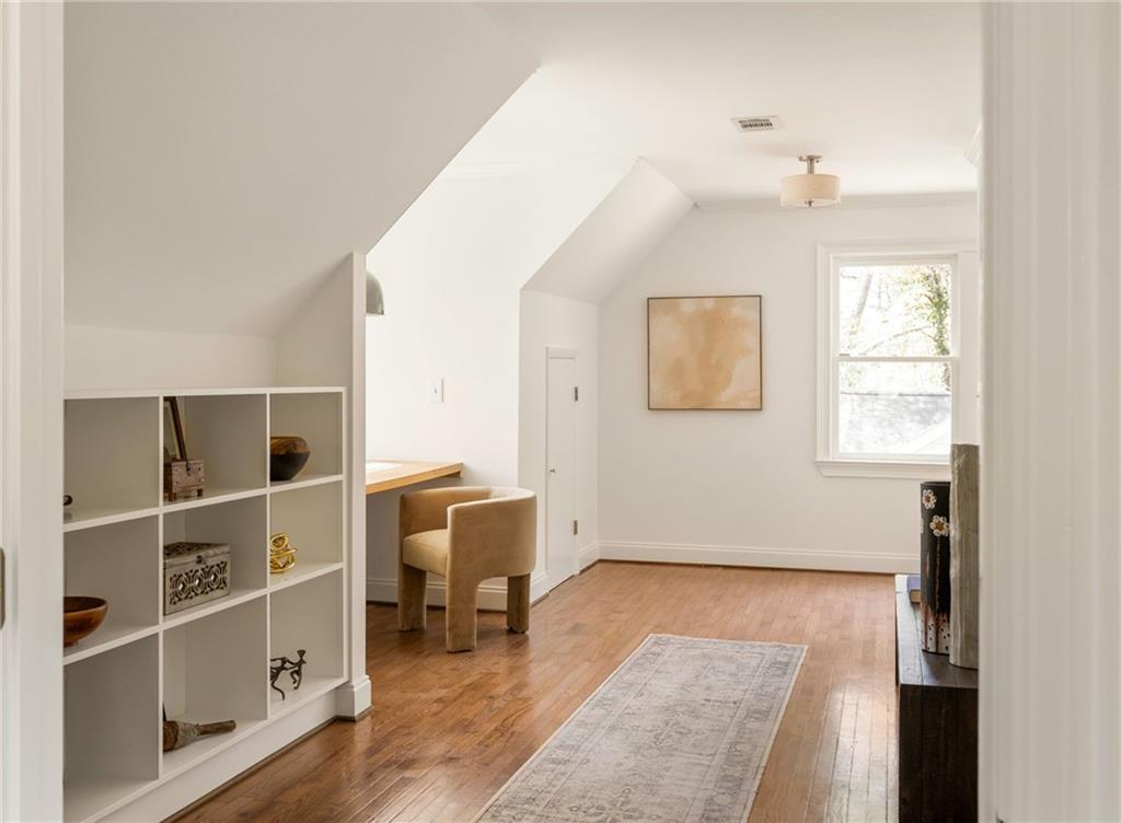 Bright upper-level room with sloped ceilings, hardwood floors, built-in cubby shelving, and a small desk.