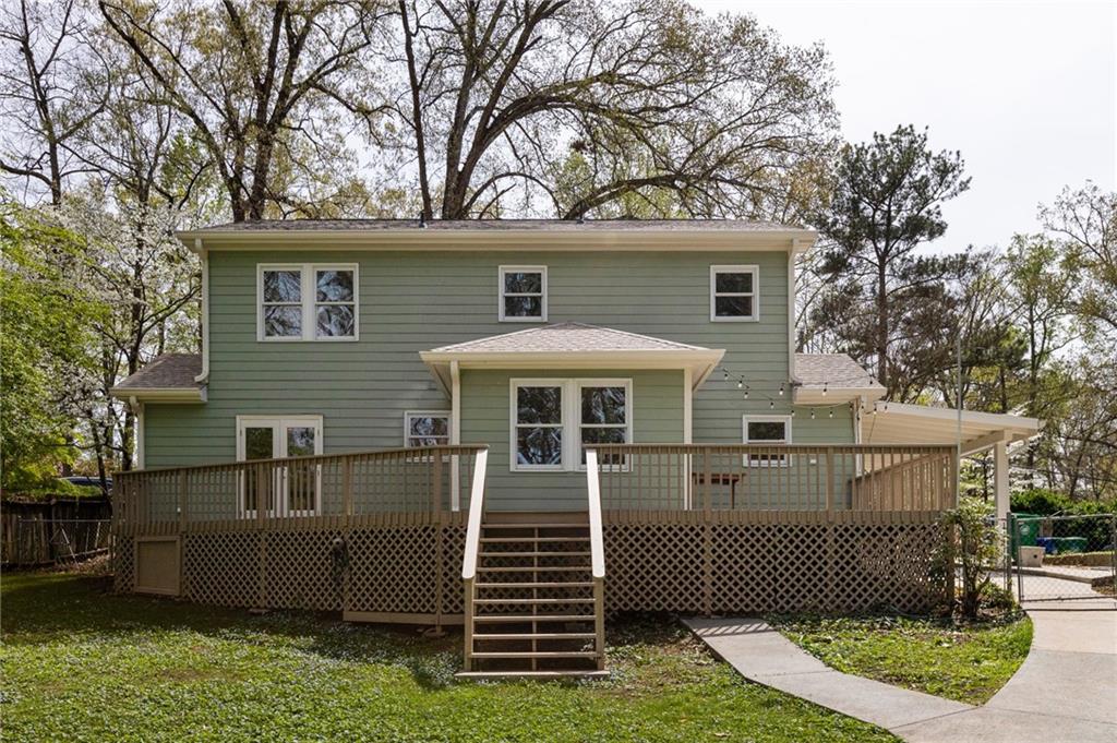 Sage-green two-story house with a large raised deck and central stairs.