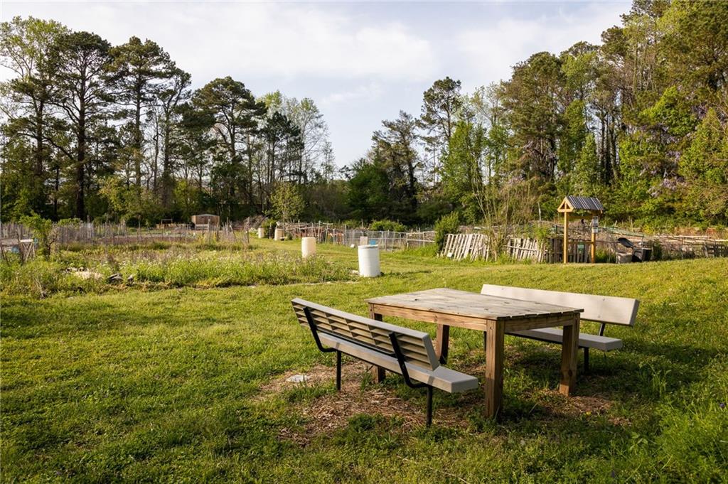 Grassy yard with a picnic table and benches beside fenced garden plots and woods.
