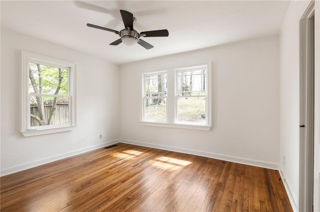 Empty bedroom with hardwood floors, a ceiling fan, and three windows.
