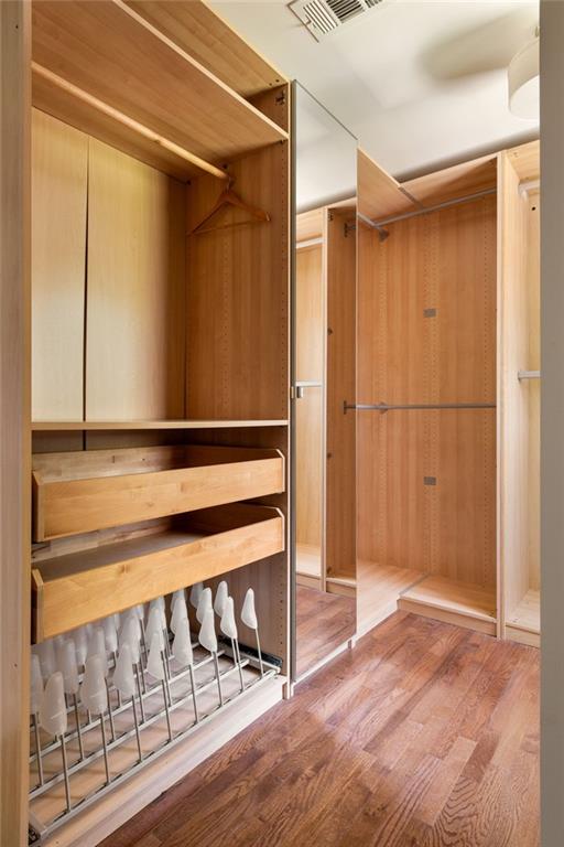 Walk-in closet with warm wood cabinetry, pull-out drawers, shoe racks, and hardwood flooring.