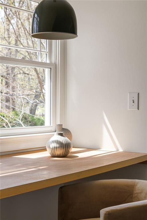 Desk nook beside a large window, with a striped vase, black pendant light, and upholstered chair.
