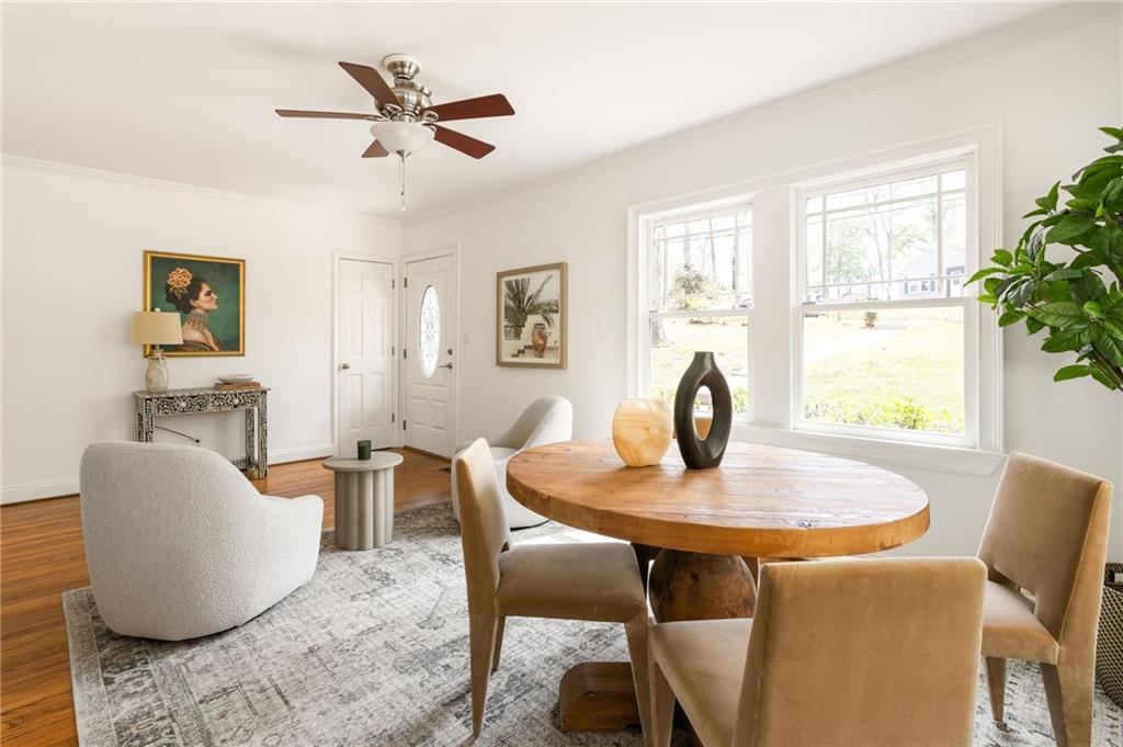 Bright dining area with a round wood table, upholstered chairs, and large windows.