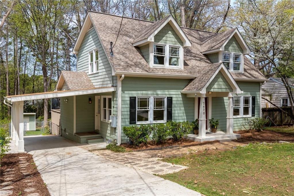 Sage green two-story house with dormer windows, a covered carport, and a concrete driveway.