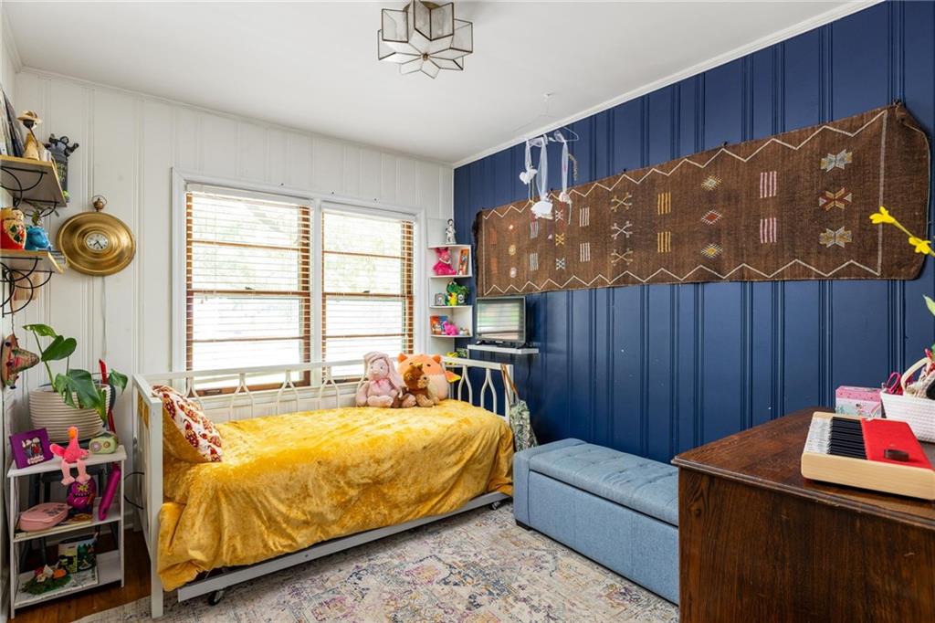 Bedroom with a mustard-yellow bedspread, blue paneled wall, large windows, and a desk with a keyboard.