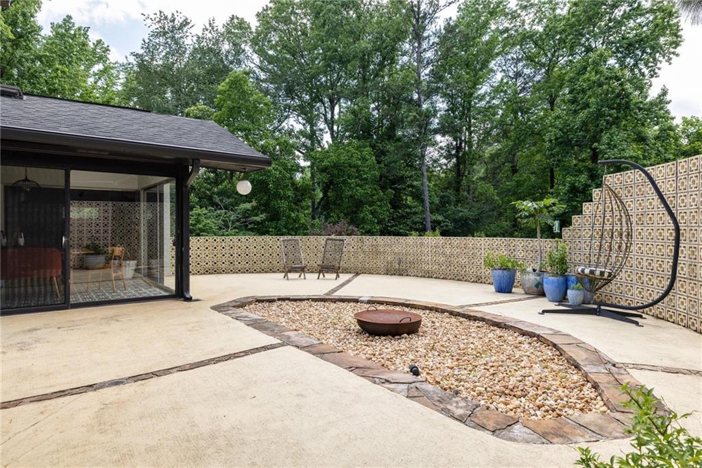 Backyard patio with a gravel fire-pit area, patterned privacy walls, and a hanging egg chair.