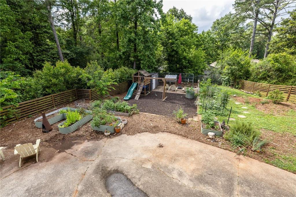 Backyard patio with raised garden beds and a wooden playset beneath mature trees.