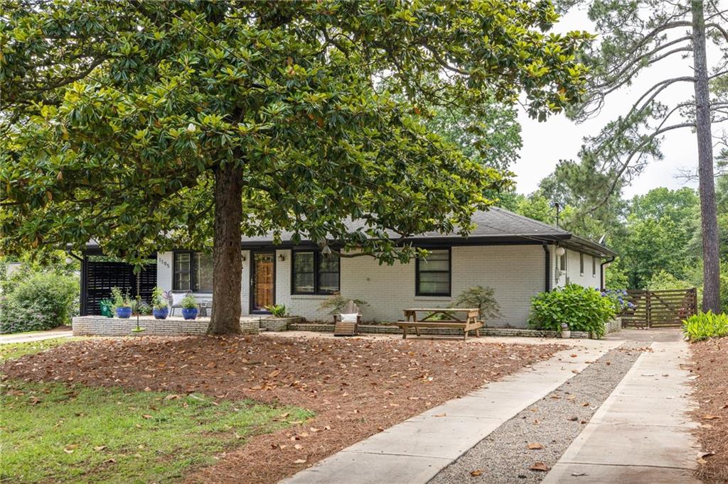 Single-story brick home beneath a large shade tree, with a concrete driveway and patio seating.