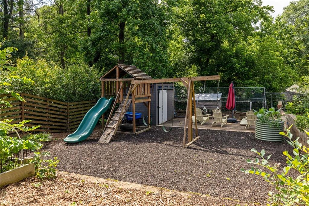 Wooded backyard with a wooden playset, green slide, swings, and outdoor seating.