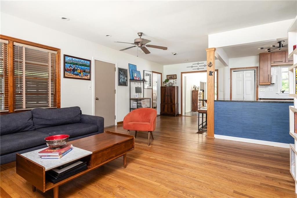 Living room with hardwood floors, a dark blue sofa, orange chair, and open kitchen with blue peninsula.