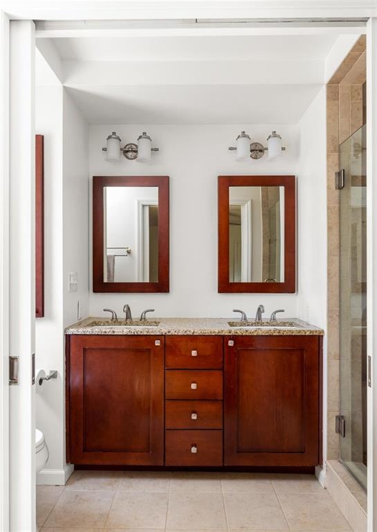 Bathroom with a double vanity, wood cabinets, matching mirrors, and a glass-enclosed shower.