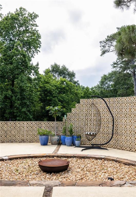 Patio with a gravel fire pit, hanging chair, blue planters, and patterned privacy wall.