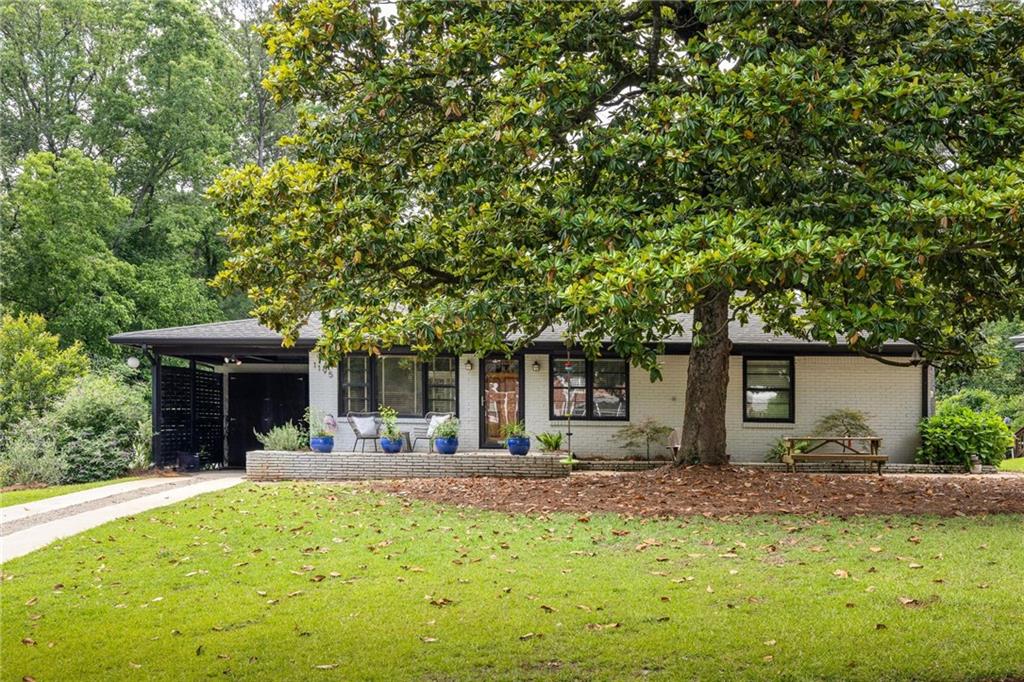 White-brick single-story home shaded by a large magnolia tree, with a broad lawn and covered carport.